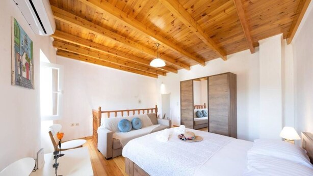 Un dormitorio con techo de madera, una cama con ropa de cama blanca, una mesita de noche y una silla.