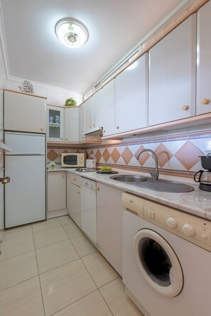 A compact kitchen with white cabinets, a built-in microwave, a sink, and a washing machine. - Beachfront Apartment with Sea Views in Tamarindos Benalmádena (Benalmádena)