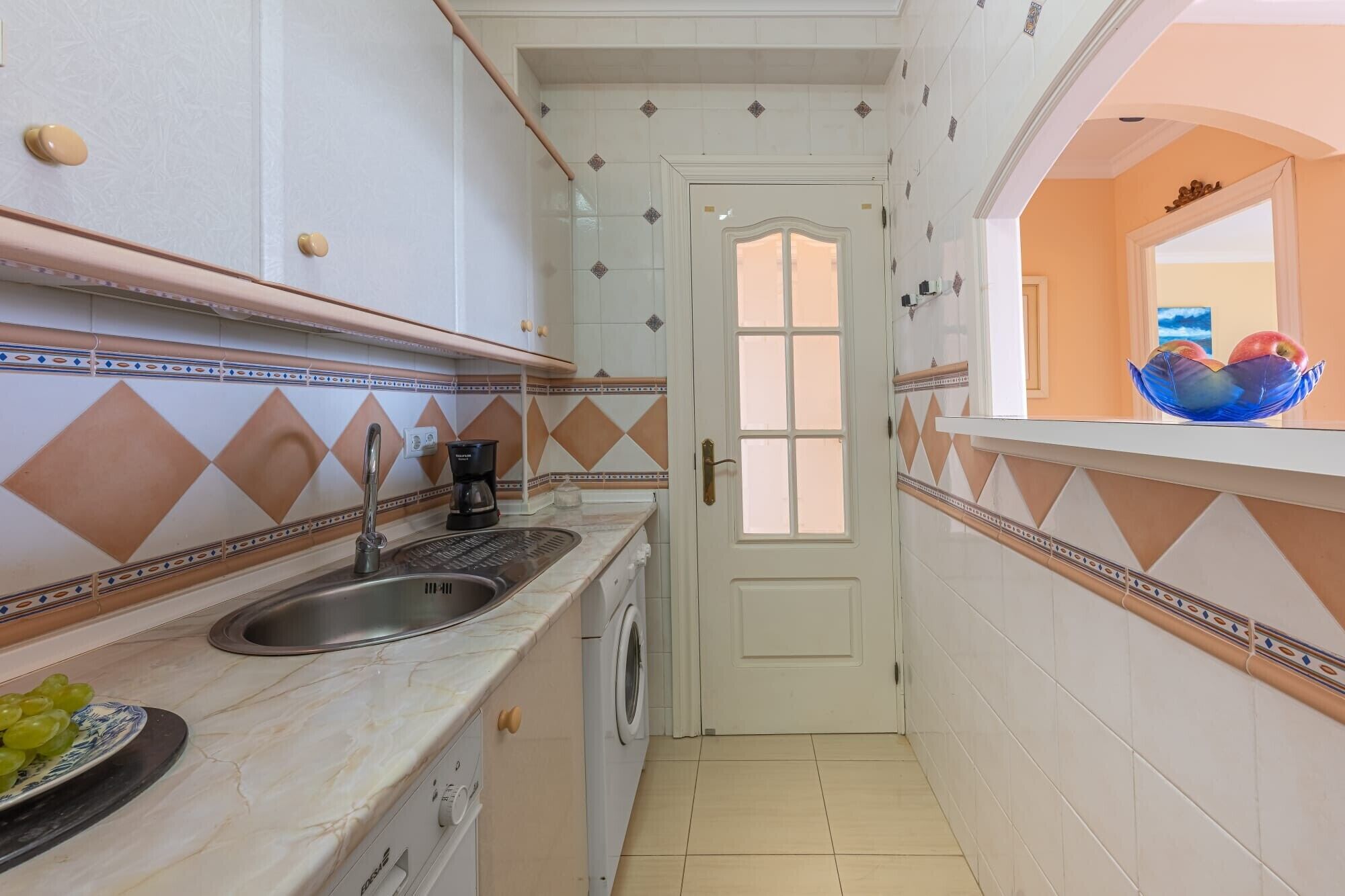 A narrow kitchen with a sink, a coffee maker, and a washing machine.