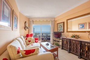 A living room with a sofa, a coffee table, a TV, and a cabinet. There is a balcony with a view of the sea. - Beachfront Apartment with Sea Views in Tamarindos Benalmádena (Benalmádena)