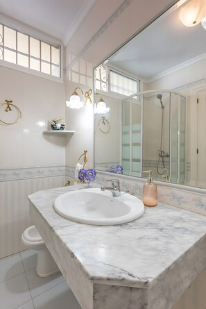 Une salle de bain avec un lavabo en marbre blanc, un grand miroir et un espace douche.