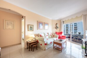 A living room with a sofa, a red chair, a coffee table, and a balcony with a view of high-rise buildings. - Beachfront Apartment with Sea Views in Tamarindos Benalmádena (Benalmádena)