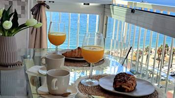 Et bord med appelsinjuice, et croissanter og en kop kaffe, med udsigt over en strand og havet.