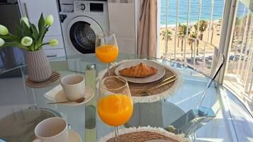 Morgenmad på en balkon med udsigt til havet, med croissanter, appelsinjuice og kaffe.