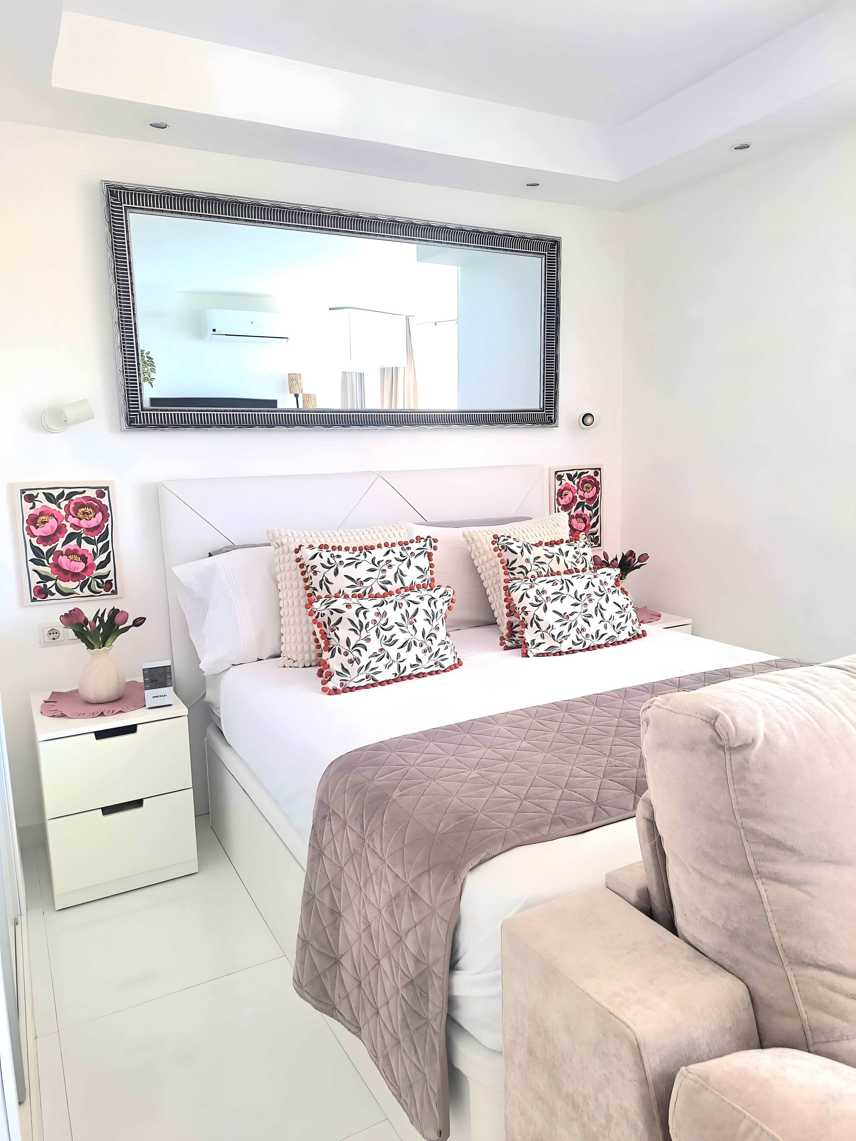 Un dormitorio con cama, mesitas de noche, una silla y un espejo grande.