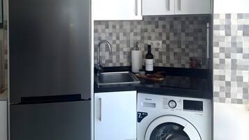 Une cuisine compacte dotée d’un réfrigérateur en acier inoxydable, d’un lave-linge et d’un dosseret carrelé.