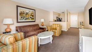 Habitación de hotel con un sofá de cuero marrón, sillones a rayas, una pequeña mesa de centro blanca, un cuadro en la pared y una zona de kitchenette.