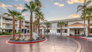 Un hotel con una recepción, palmeras y un patio bien cuidado.