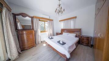 A bedroom with a wooden bed, a dresser, a nightstand, a chandelier, and a large mirror.