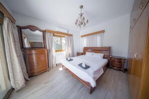 Un dormitorio con una cama de madera, un aparador, una mesita de noche, una araña y un espejo grande.