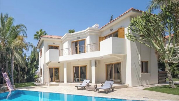 Uma casa de dois andares com piscina, varanda e palmeiras.