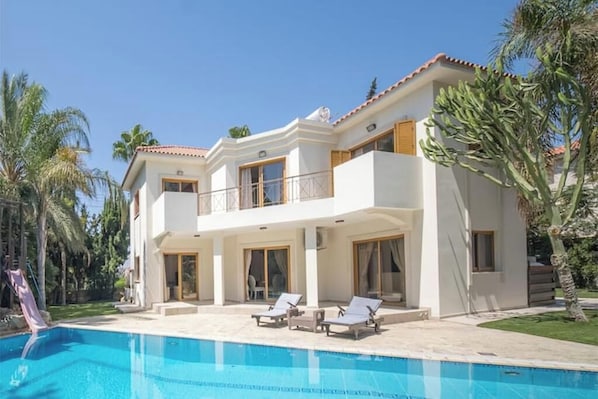 Una casa de dos pisos con piscina, balcón y palmeras.