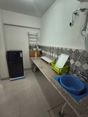 A compact kitchen with a refrigerator, a sink, a countertop, and a tiled backsplash. - Stylish 2 Bedroom Apartment in Gurugram (Gurugram)