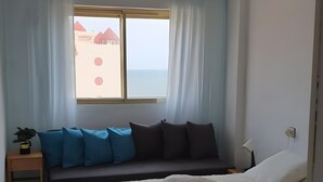 Ein Schlafzimmer mit Bett, Deckenventilator, Fenster mit Vorhängen, Nachttisch und Beistelltisch.