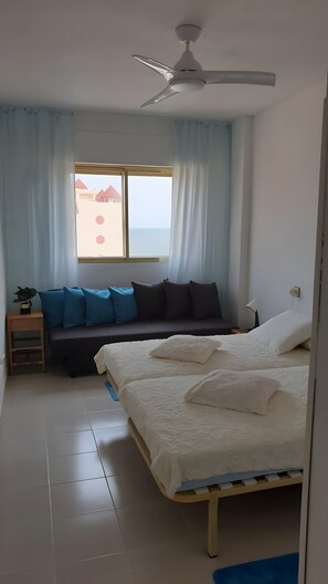 A bedroom with a bed, a ceiling fan, a window with curtains, a bedside table, and a nightstand.