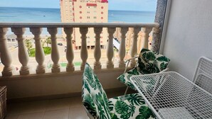 Ein Balkon mit Tisch und Stühlen, Blick aufs Meer und ein Gebäude im Hintergrund.