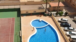 Ein mehrstöckiges Hotel mit Schwimmbad, Tennisplatz und Meerblick.