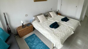 A bedroom with a bed, a ceiling fan, a nightstand, a lamp, a painting, and a blue rug.