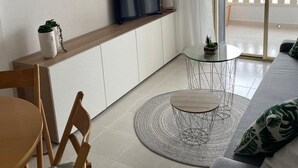 A modern living space with a sofa, a dining table, a TV on a shelf, and a balcony with a railing.