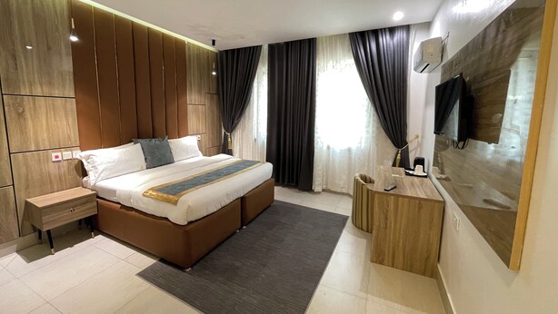 A modern bedroom with a large bed, bedside tables, a desk, and a TV mounted on the wall.