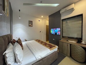 Una habitación de hotel con cama, escritorio, televisor y aire acondicionado.