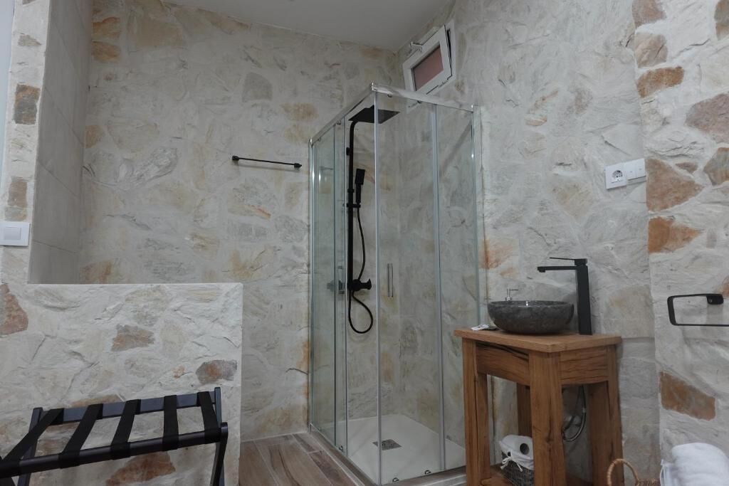 Ducha con puertas de vidrio, banca de madera y pared de piedra.