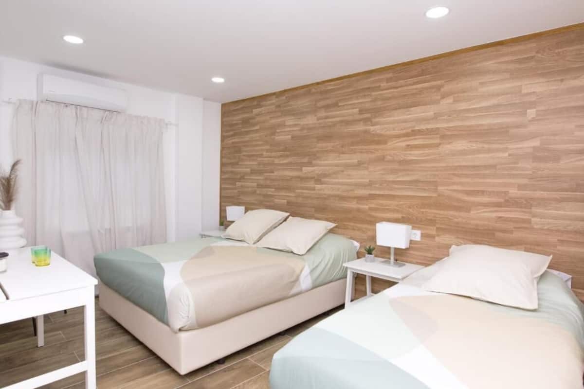 Una habitación de hotel moderna con dos camas, una pared decorativa de madera, una mesita de noche blanca y una pequeña mesa con lámpara.