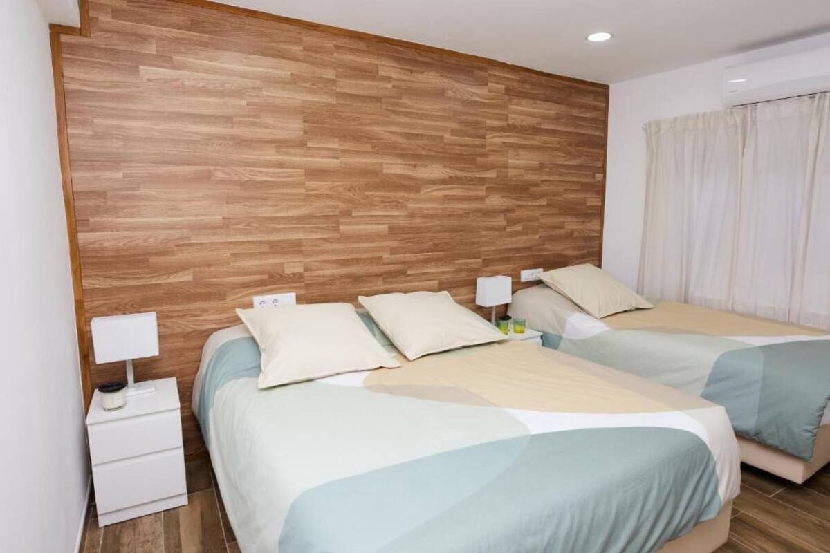Habitación de hotel con dos camas, cabecero de madera, mesitas de noche con lámparas y una ventana con cortinas.