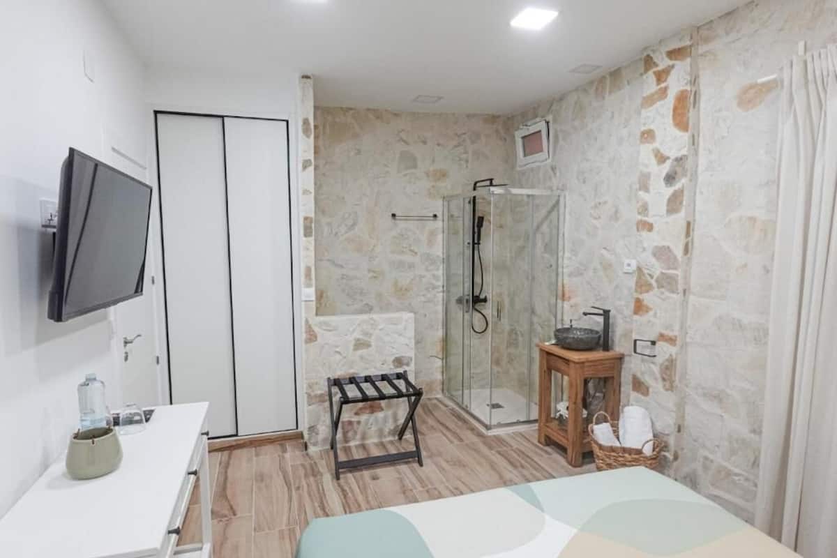 Un baño con ducha, lavamanos, espejo y televisión montada en la pared.