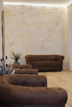 A room with a brown sofa, a potted plant, and a textured wall.