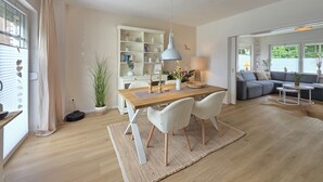 Ett modernt vardagsrum med en matplats, en soffa, en lampa och en bokhylla.
