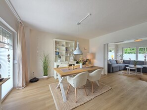 Una sala de estar moderna con comedor, sofá, lámpara y estantería.