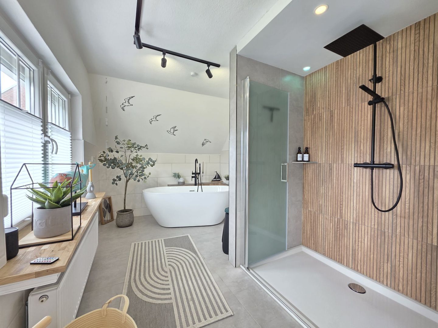 Ein modernes Badezimmer mit einer freistehenden Badewanne, einer Dusche inklusive Handbrause, einer Duschkabine aus Glas und einer Wandverkleidung aus Holz.