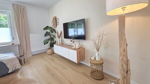 Ett modernt vardagsrum med en platt-TV, trägolv, en soffa, ett soffbord och en lampa.