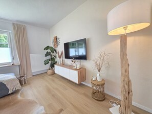 Una sala de estar moderna con televisor de pantalla plana, piso de madera, un sofá, una mesa de centro y una lámpara.
