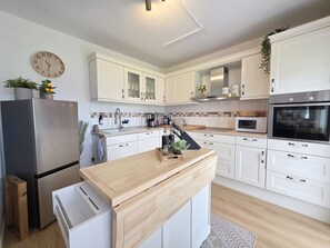 Una cocina moderna con armarios blancos, encimera de madera, refrigerador de acero inoxidable, microondas y horno.