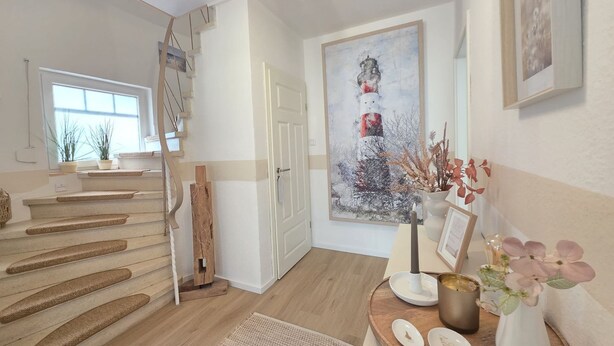 En hall med en trappa, en målning av en fyr och ett litet bord med dekorativa föremål.