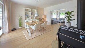 Ett rymligt vardagsrum med ett matbord, stolar, en soffa, en svart spis och en bokhylla.