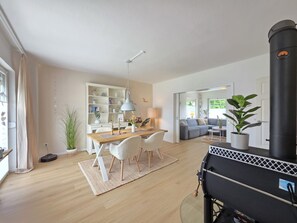 Un amplio espacio habitable con una mesa de comedor, sillas, un sofá, una estufa negra y una estantería.