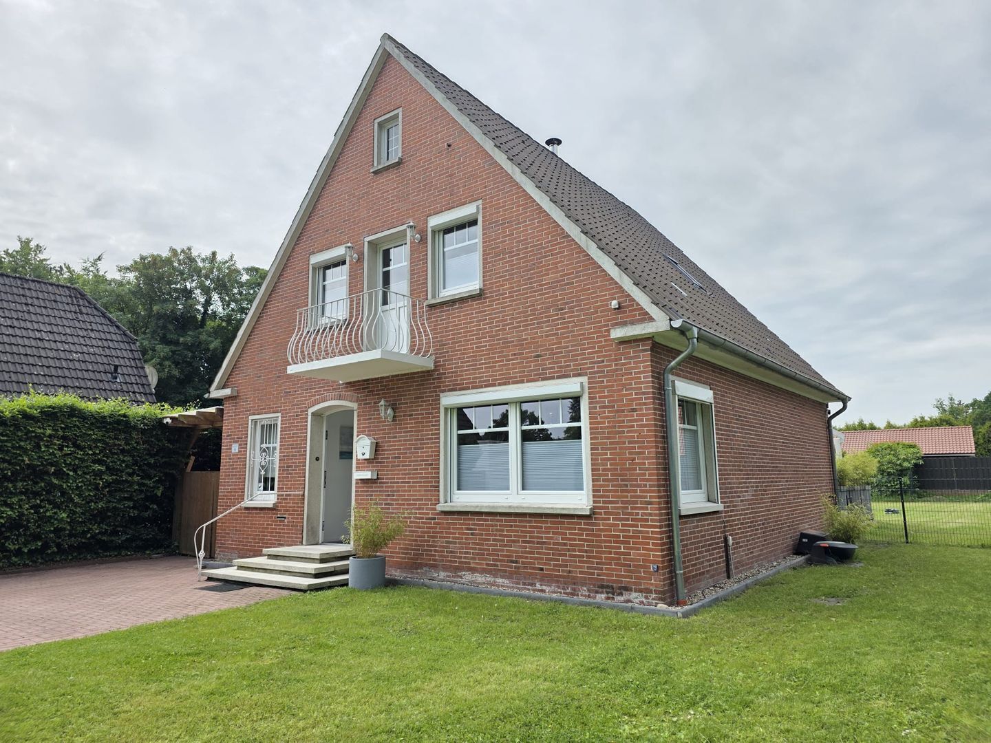 Ein zweistöckiges Ziegelhaus mit Balkon, Eingangstür und kleinem Vorgarten.