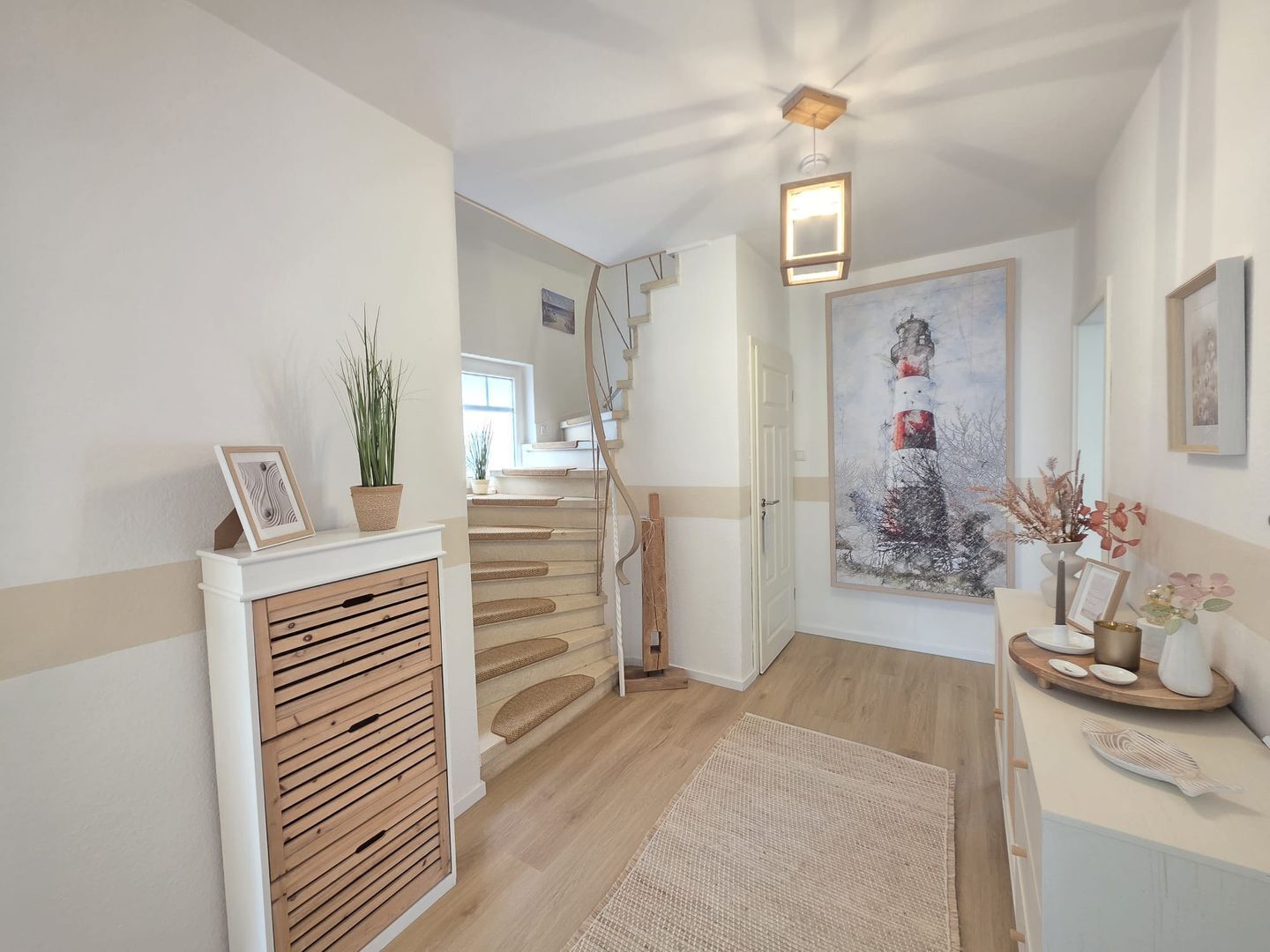 Un couloir avec un escalier, une cheminée, un tableau et une petite table ornée d’objets décoratifs.