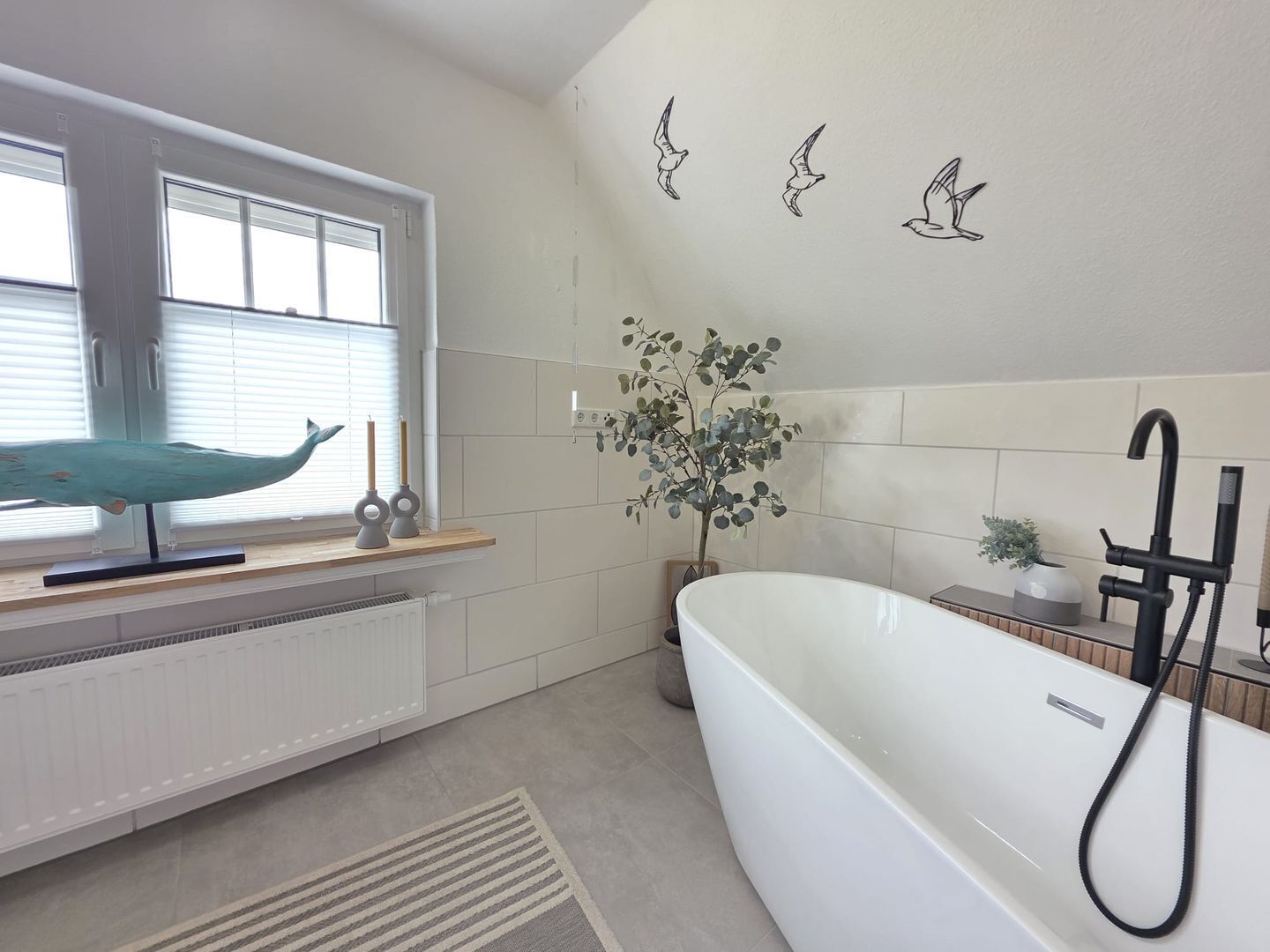 Une salle de bain moderne avec une baignoire sur pieds, une fenêtre avec des stores, un radiateur et une plante décorative.