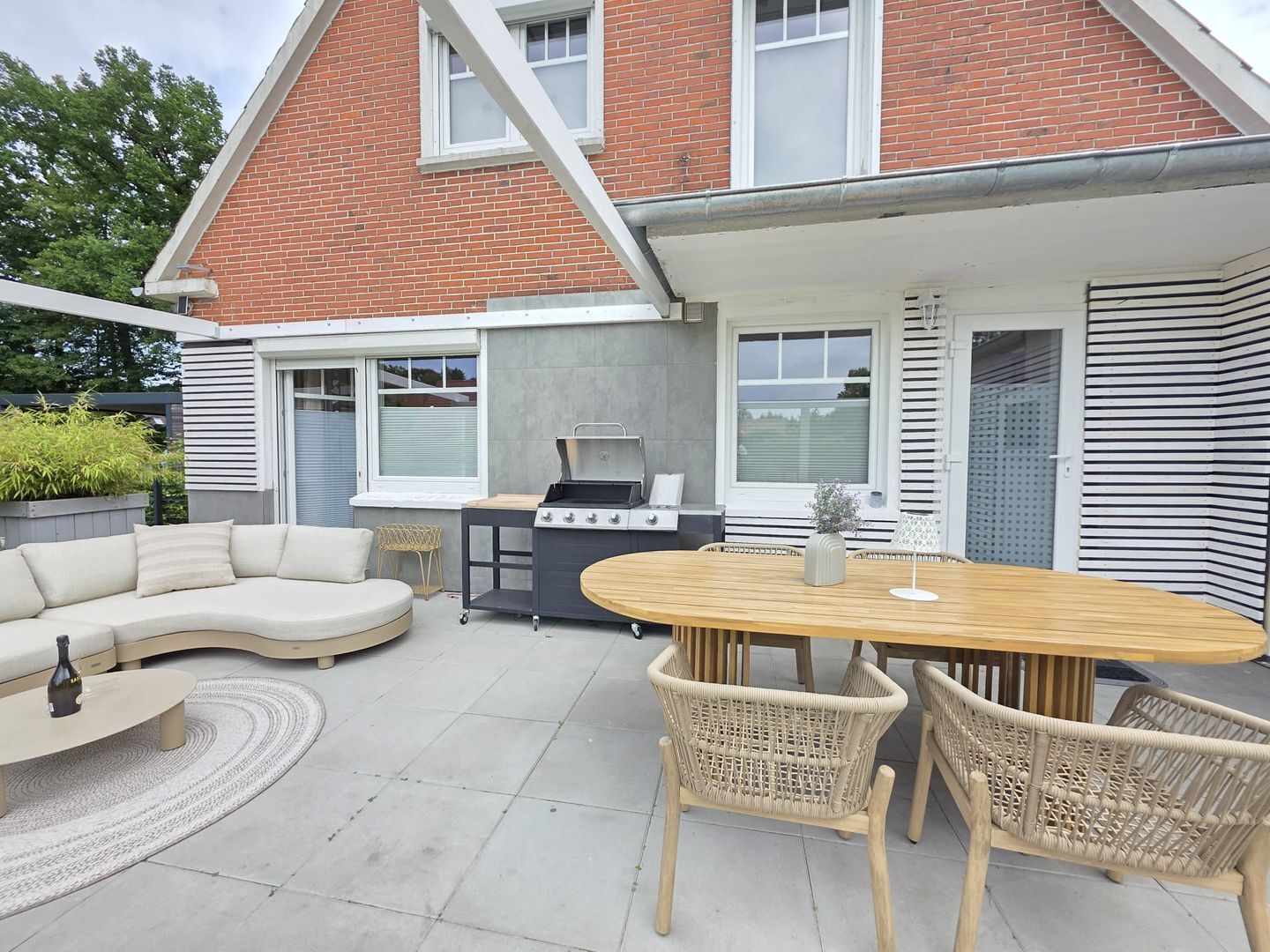 A patio with a round table, wicker chairs, a sofa, and a grill.