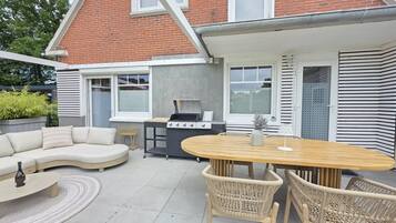 A patio with a round table, wicker chairs, a sofa, and a grill.