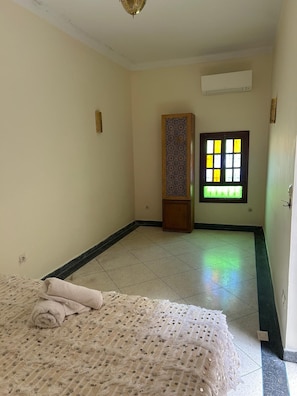 Una habitación con cama, ventana con diseño geométrico y aire acondicionado en la pared.
