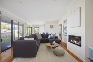 Een moderne woonkamer met een hoekbank, een open haard en een groot raam.