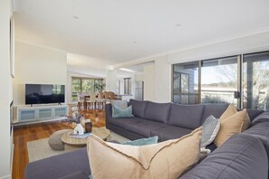 A modern living room with a large grey sofa, a flat-screen TV, and a dining area with chairs and a table. - Rye Coastal Oasis. (Blairgowrie)