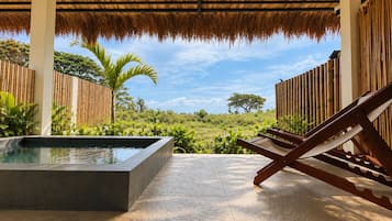 A covered outdoor area with a pool, lounge chairs, and a view of a natural landscape.