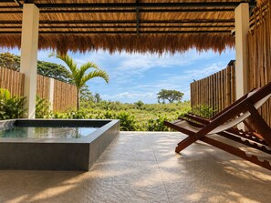 A covered outdoor area with a pool, lounge chairs, and a view of a natural landscape.