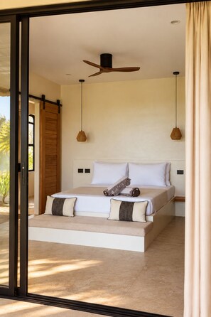 A bedroom with a large bed, a ceiling fan, and a view through a glass door.